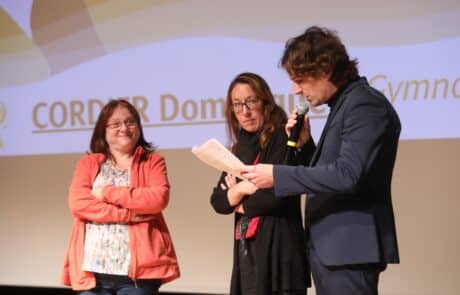 l'animateur micro est en action, entourée de deux participantes de l'événement sur scène, toutes les deux des femmes. Elle sont récompensées pour leur travail et présenter par l'animateur speaker.