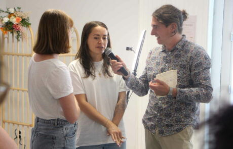 L'animateur Dominique Lowe sur la droite de la photo tient un micro en main et interview deux personnes.