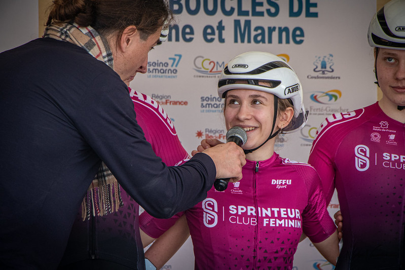 une cycliste avec son casque est interviewée par un journaliste avant le début d'une épreuve